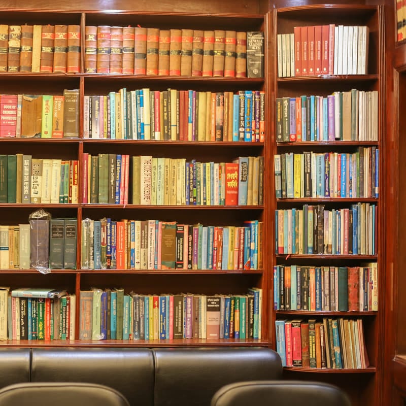 The far end of the library wall, shelves of law reports and reference volumes above the bench.